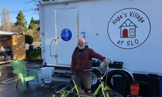 A person with a bicycle stands in front of a trailer housing Hope's Village of San Luis Obispo mobile showers