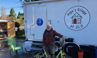 A person with a bicycle stands in front of a trailer housing Hope's Village of San Luis Obispo mobile showers
